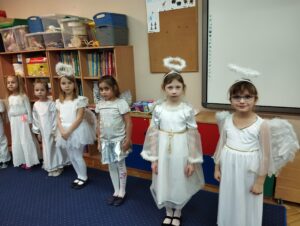 Dzieci stoją w rzędzie przebrane za aniołki i śpiewają kolędę
