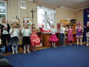 Dzieci stoją w półkolu, śpiewają piosenkę i ilustrują ją ruchem ciała