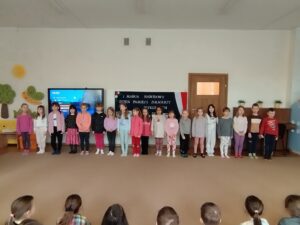 Dzieci stoją na dywanie i śpiewają hymn 5 Brygady Wileńskiej