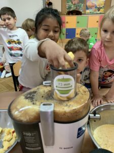 dziecko wkłada owoce do sokowirówki